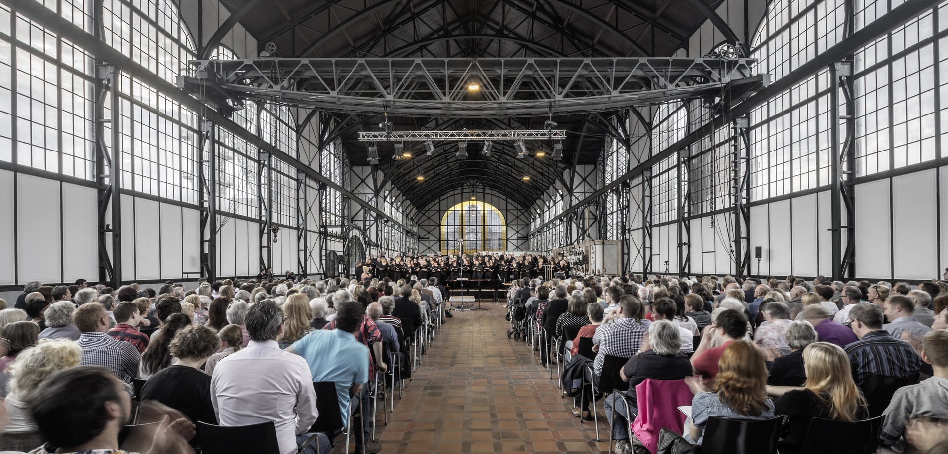 Menschen sitzen in Stuhlreihen vor einer Bühne in der Maschinenhalle von Zeche Zollern.