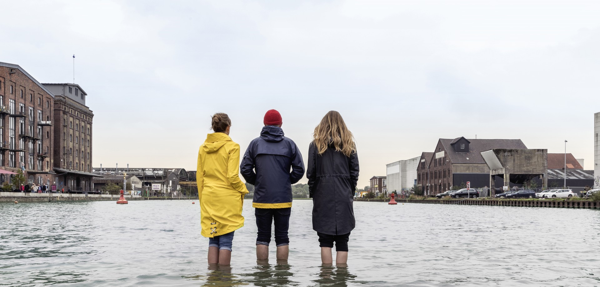 Drei Menschen stehen mit dem Rücken zur Kamera mit ihrem Füßen im Wasser im Münsteraner Hafen.